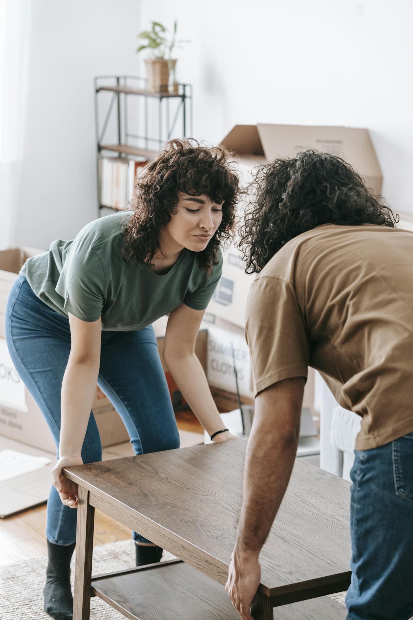 Couple lifting a wooden table while moving into a new home illuminated by daylight.